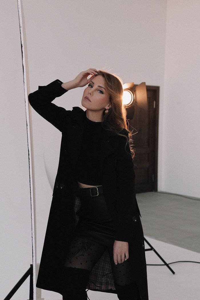 A stylish woman in a black coat and skirt posing in a professional studio setting.