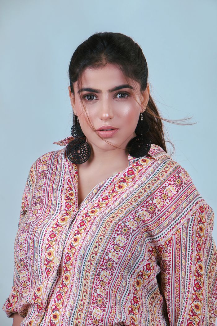 Close-up portrait of a woman wearing a floral shirt and bold earrings against a neutral background.