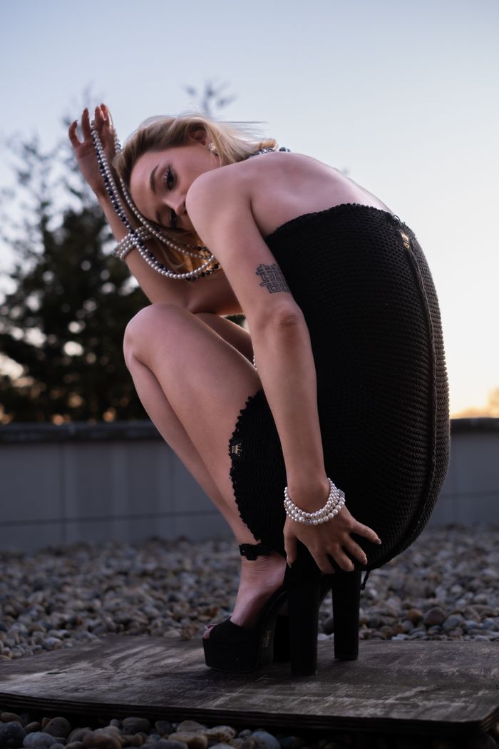 An elegant model in a black dress poses outdoors at dusk, showcasing high fashion and chic style.