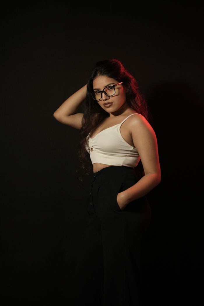 Fashionable young woman posing confidently in glasses against a dark, minimalist background.